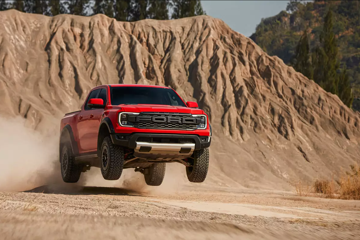 A red 2022 Ford Raptor Ranger Speeds across a desert plain kicking up dirt on a sunny day.