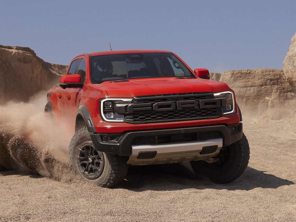 A red 2022 Ford Ranger Raptor takes a sharp turn on a dry field, kicking up a cloud of dust.