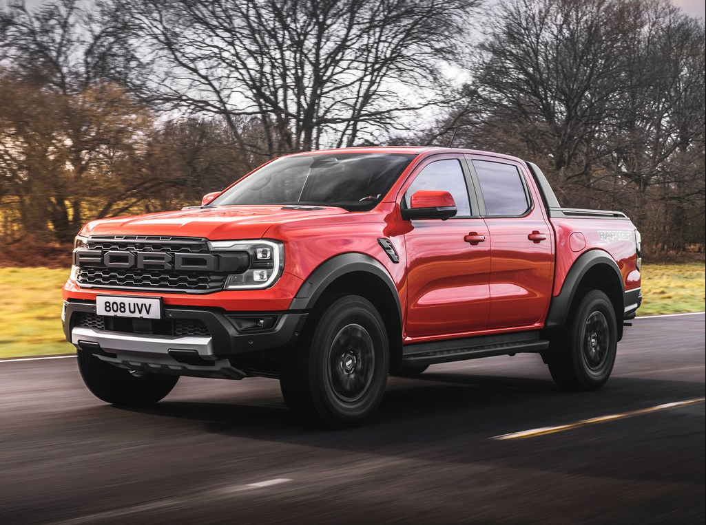 An angled profile view showing the side and grille of a red 2022 Ford Ranger Raptor as it cruises down a country highway