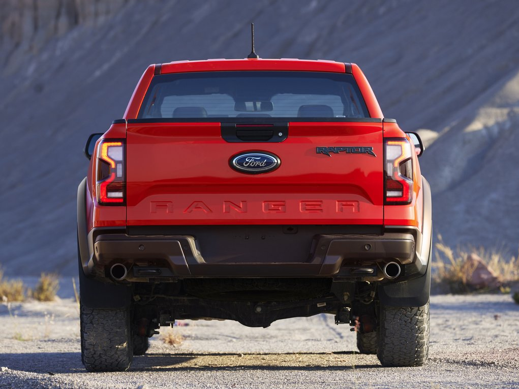 A view of the back of a red 2022 Ford Ranger Raptor as it sits parked in a dirt field surrounded by mountains.