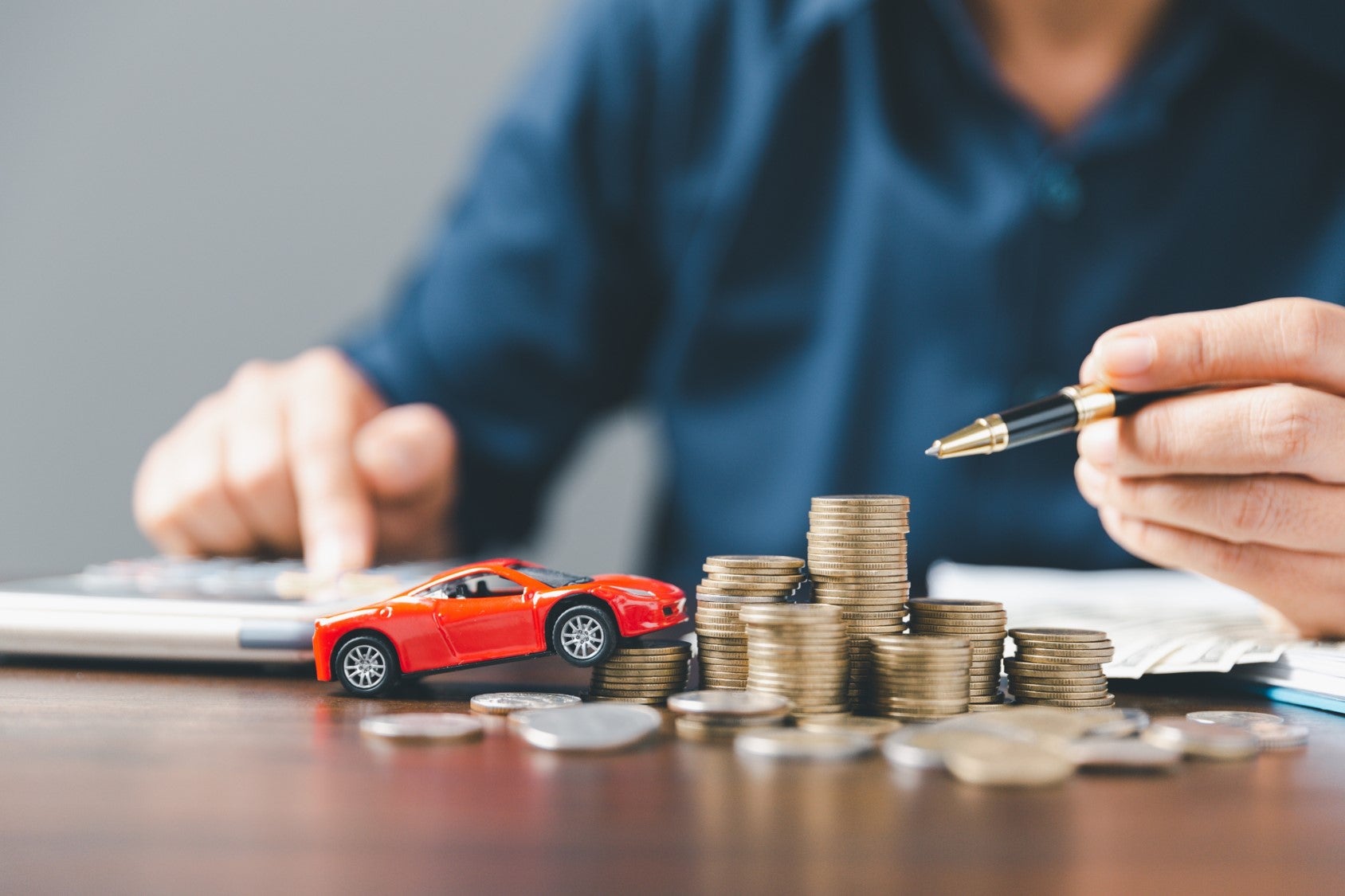 A stack of coins on a desk while a car salesman fills out paperwork for a client