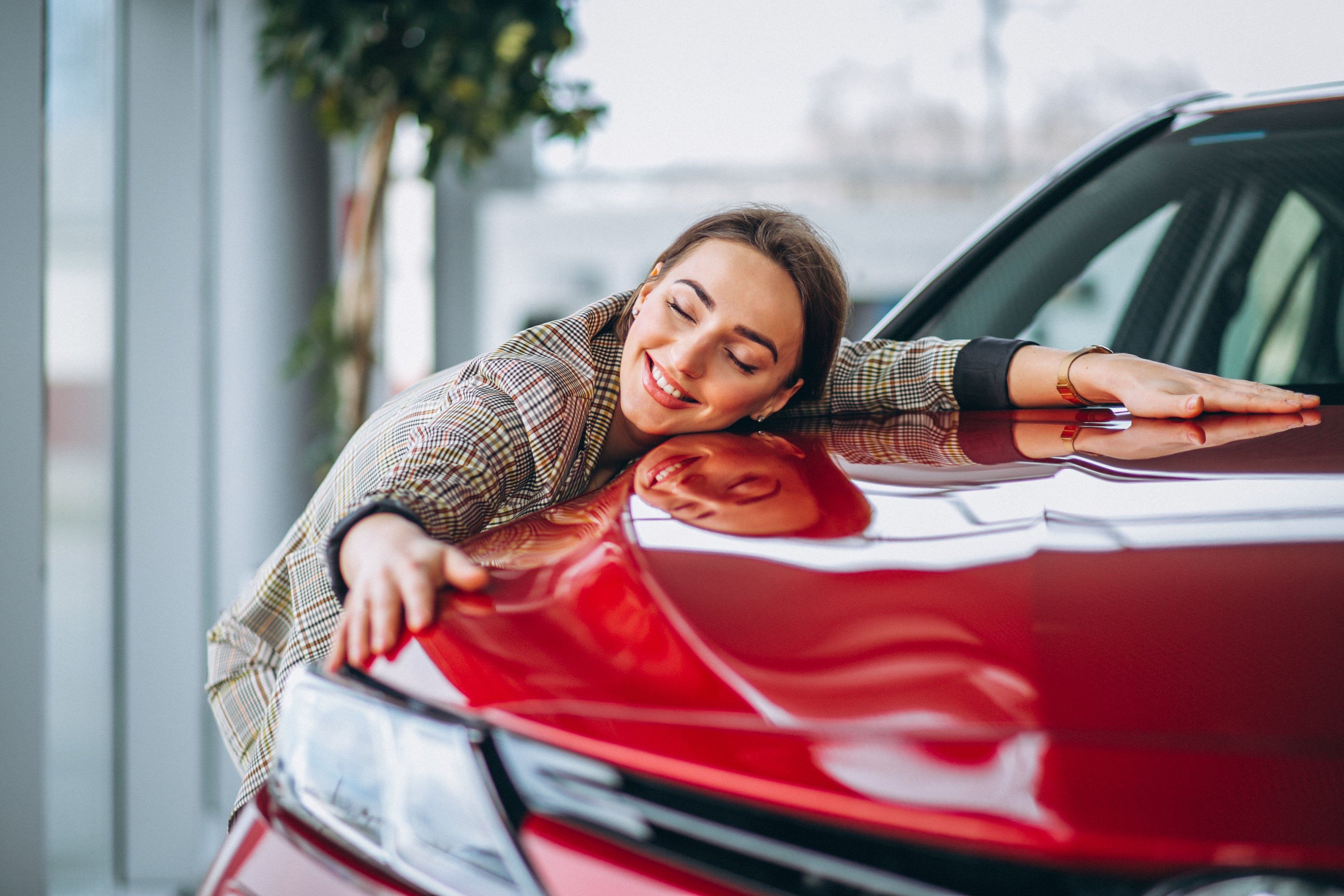 A woman hugs the fender of her new, red sports car at the dealership