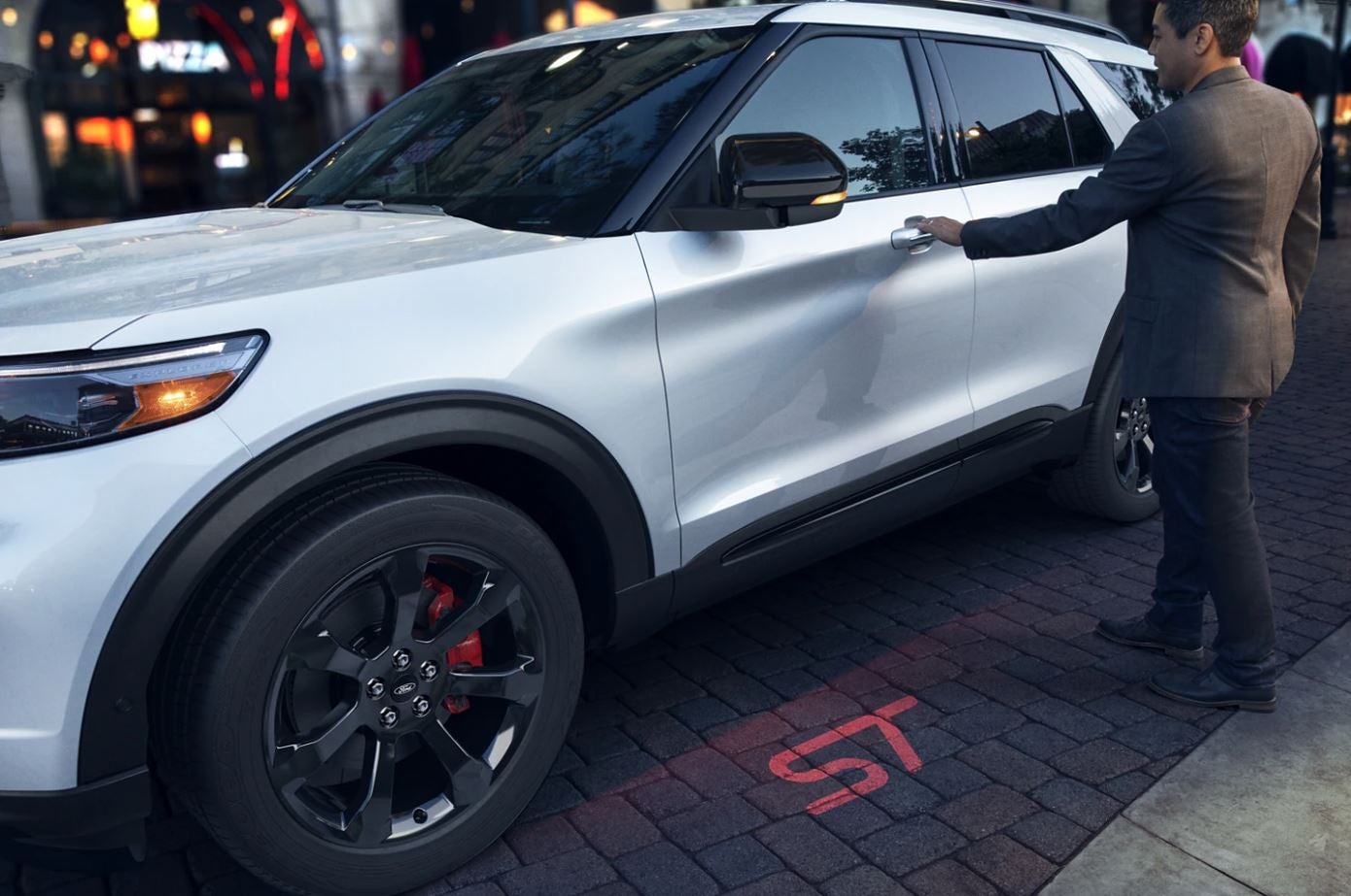 A person grabs the handle of the driver's side door to get into a white 2023 Ford Explorer ST