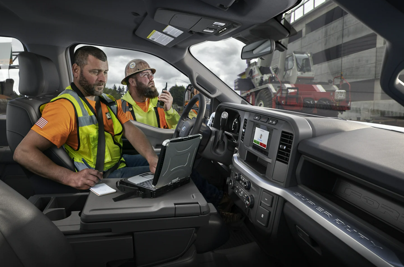 A construction worker uses the large center console in the cab of a 2023 Ford F-350 Super Duty as a work station for his laptop.