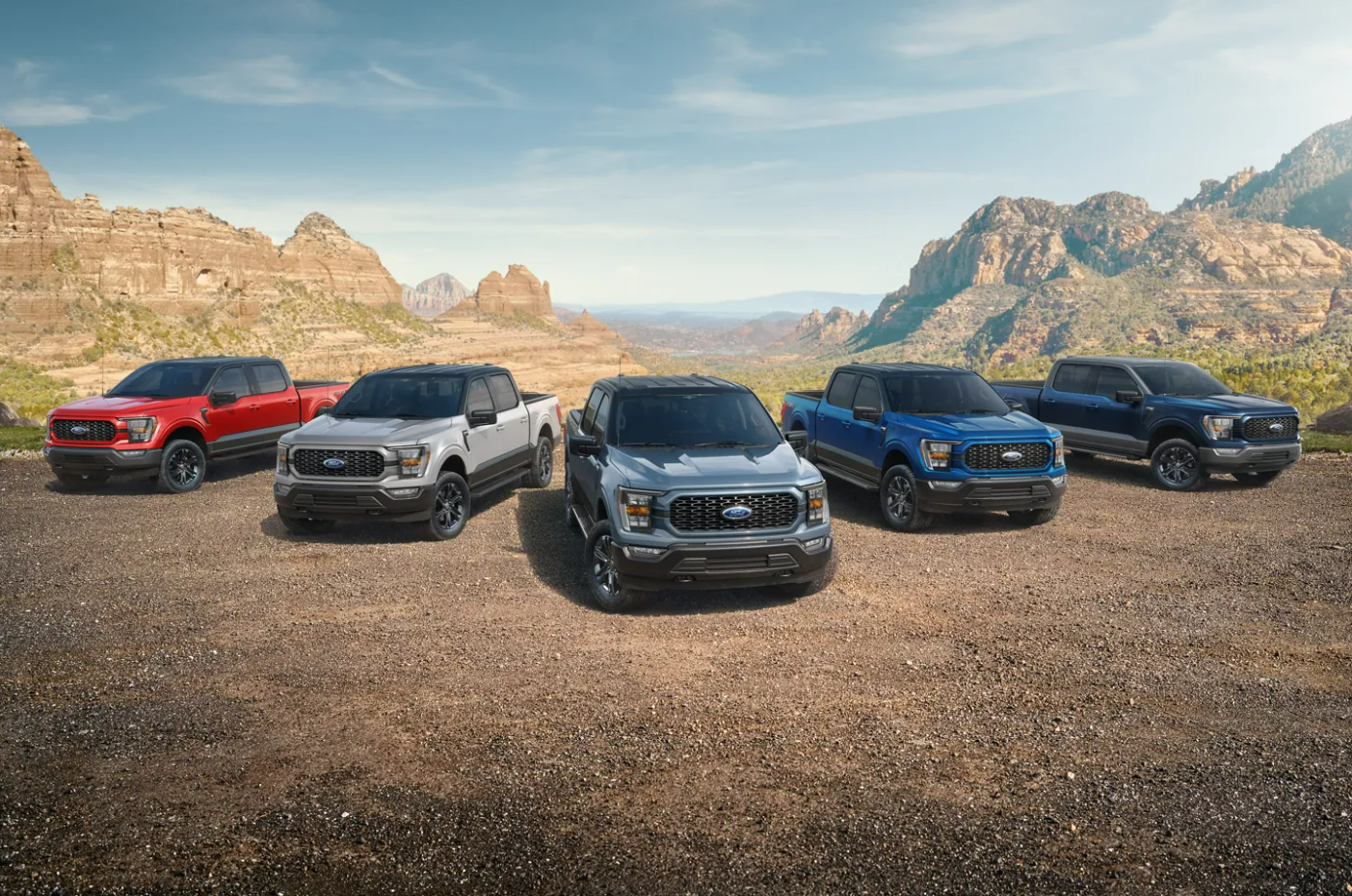 Five red, white, silver, blue, and black 2023 Ford F-150s sit parked facing the viewer on a dirt plain