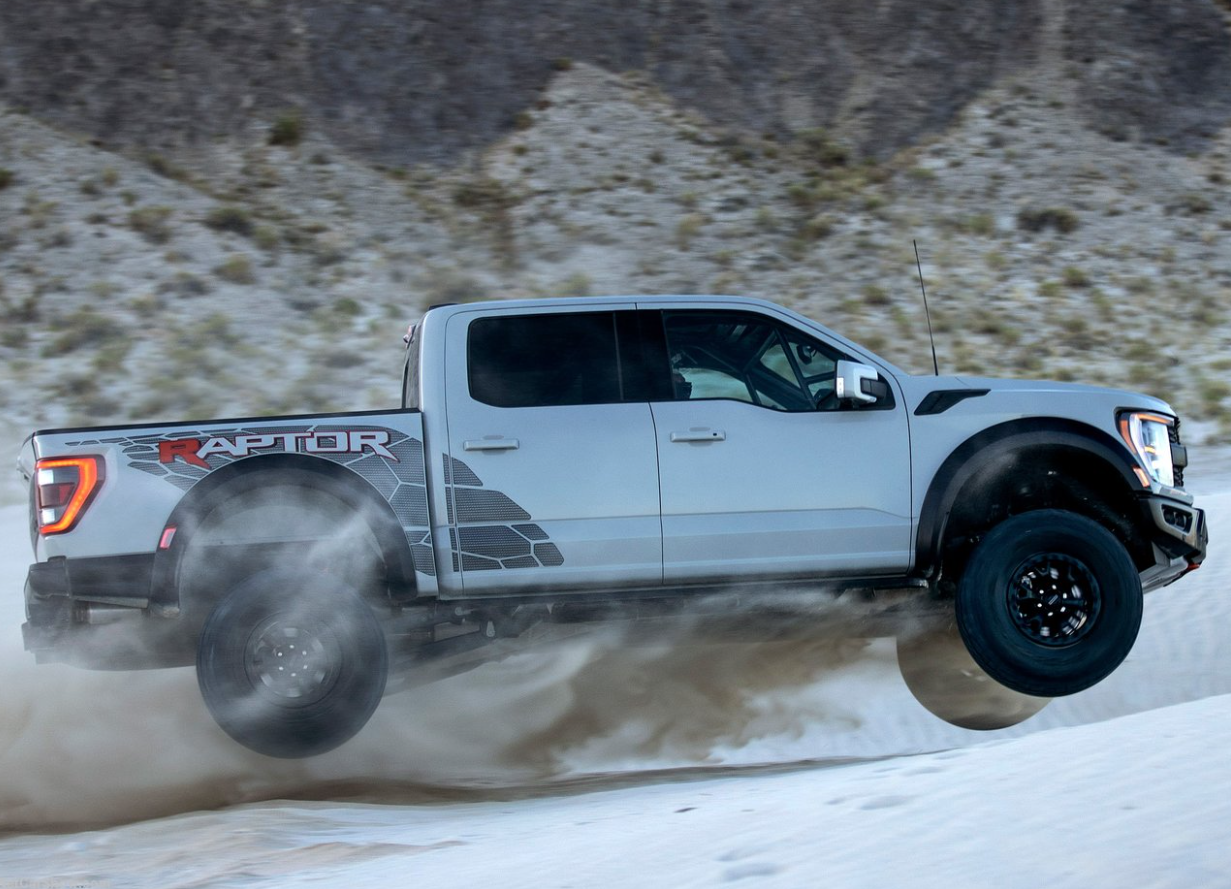 A white 2023 Ford F-150 Raptor R with side panel graphics flies through the air off-roading