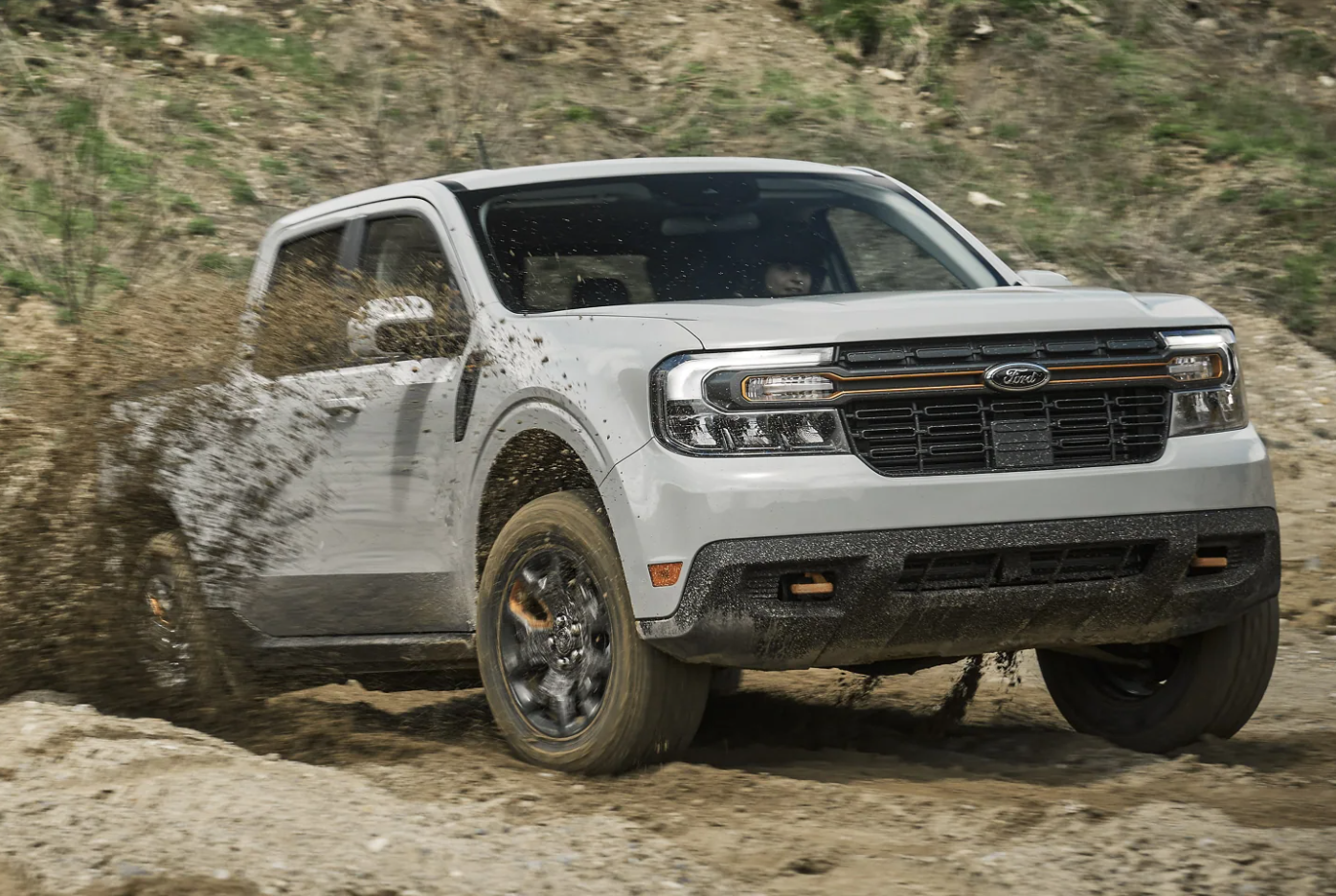 A muddy and white 2023 Ford Maverick drives through a dirt field