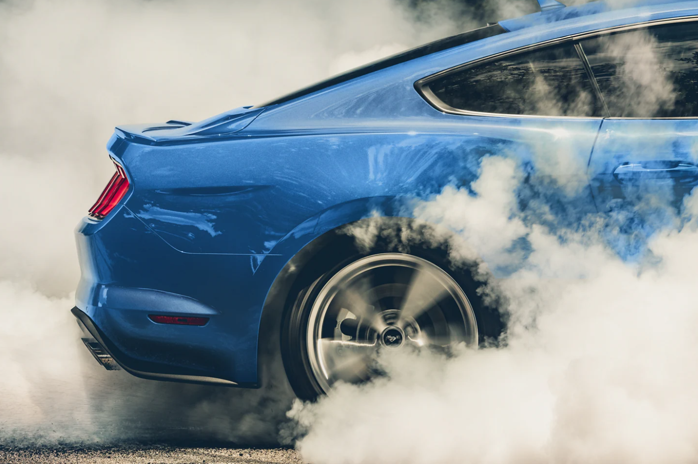 A closeup of a rear tire as it spins out on a blue 2023 Ford Mustang Mach 1