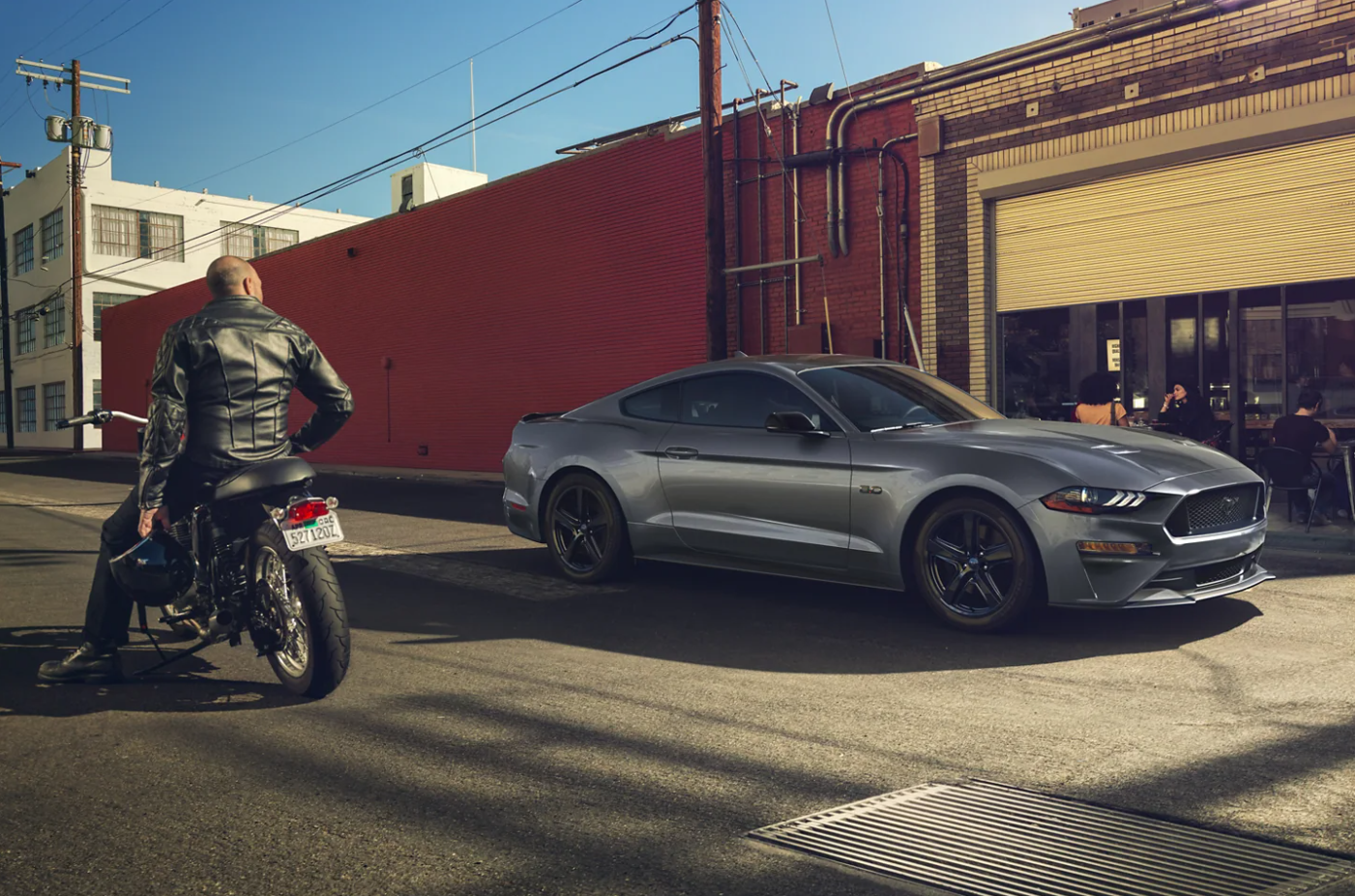 A man on a motorcycle admires a dark gray 2023 Ford Mustang