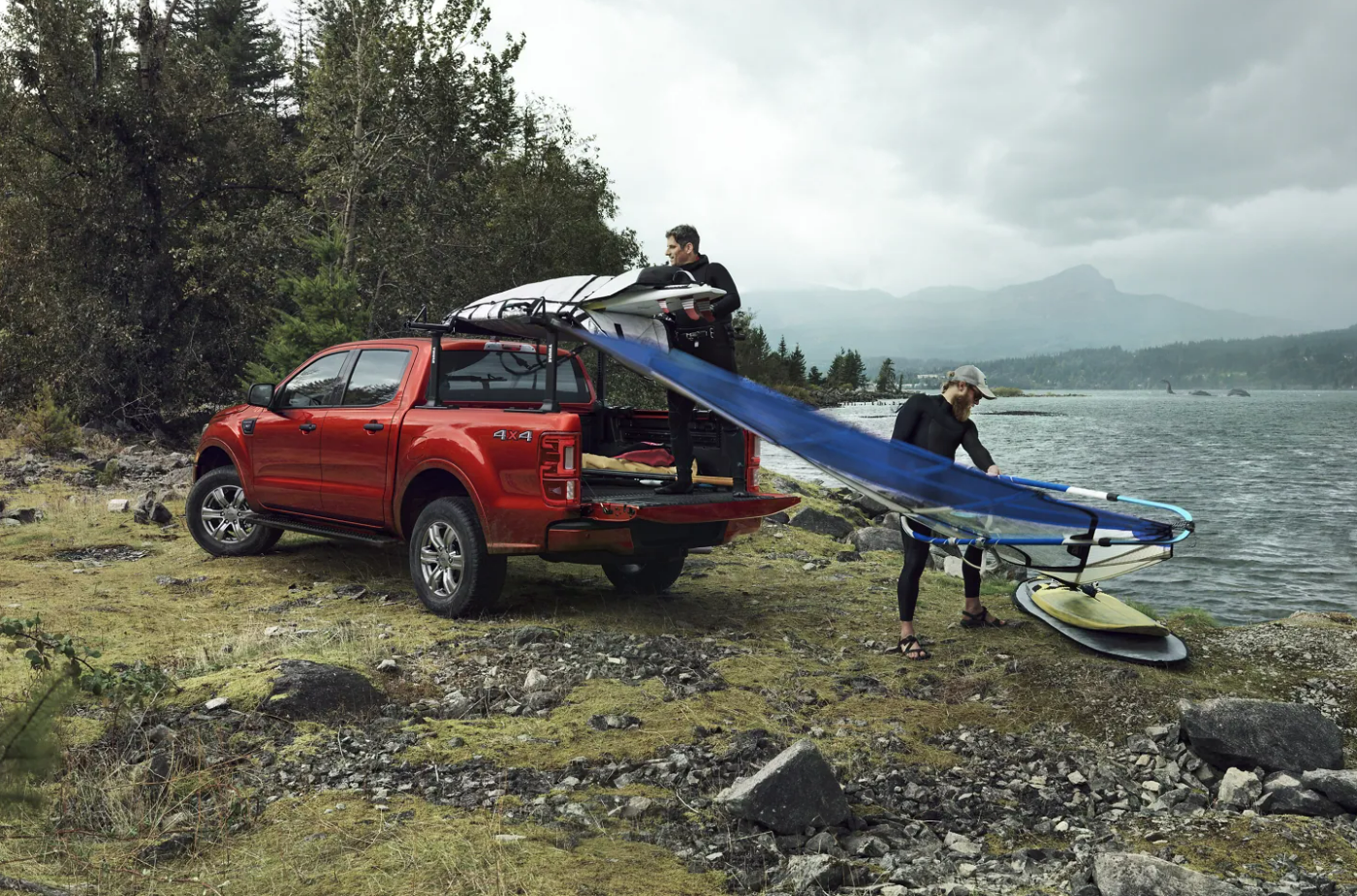 A red 2023 Ford Ranger sits parked next to a lake as a couple men unload windsurfing gear from the back