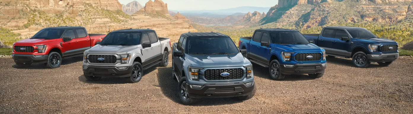 Five red, white, silver, blue, and black 2023 Ford F-150s sit parked facing the viewer on a dirt plain