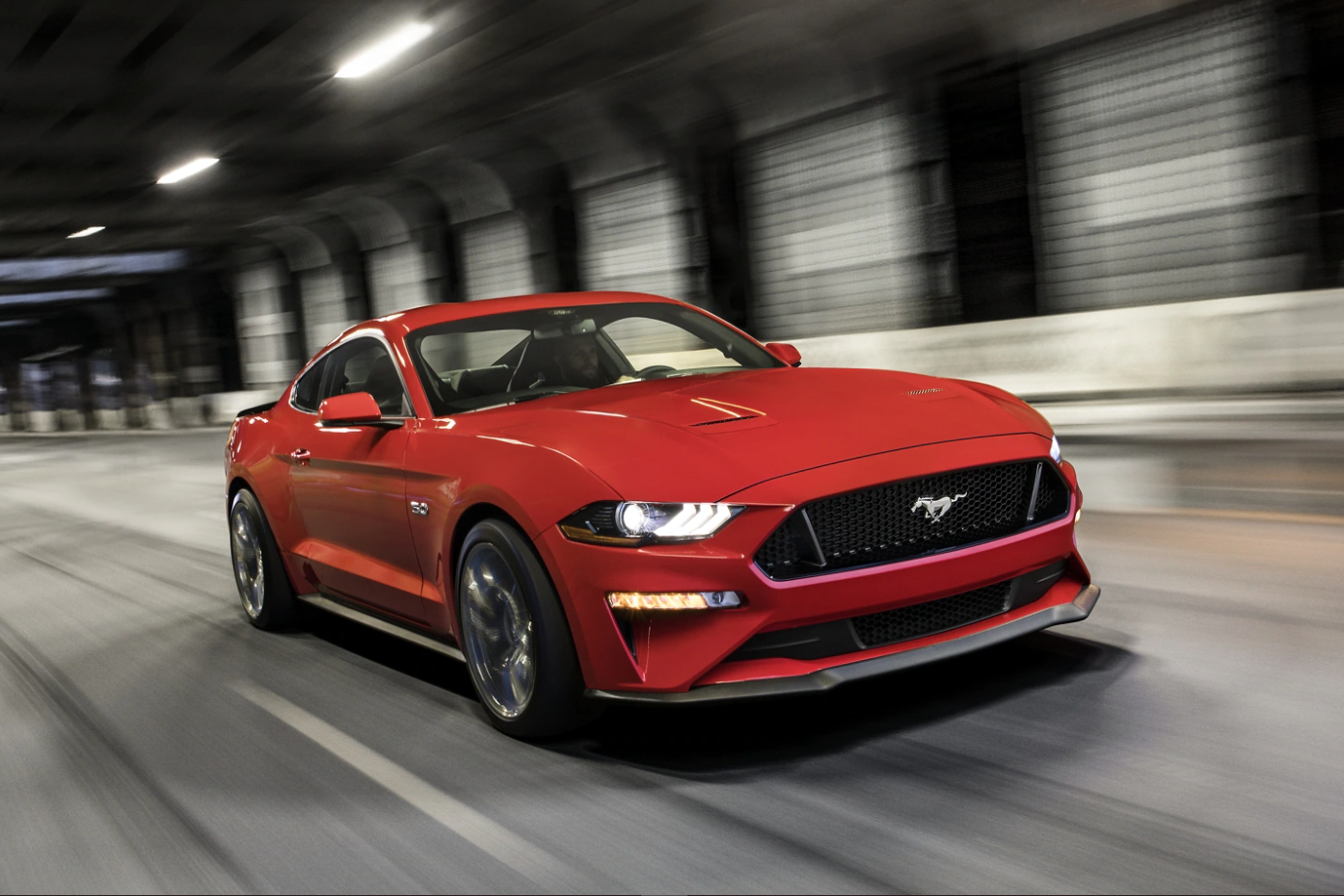 An angled view of a 2022 red Ford Mustang as it cruises down a covered city tunnel showing the grille and profile