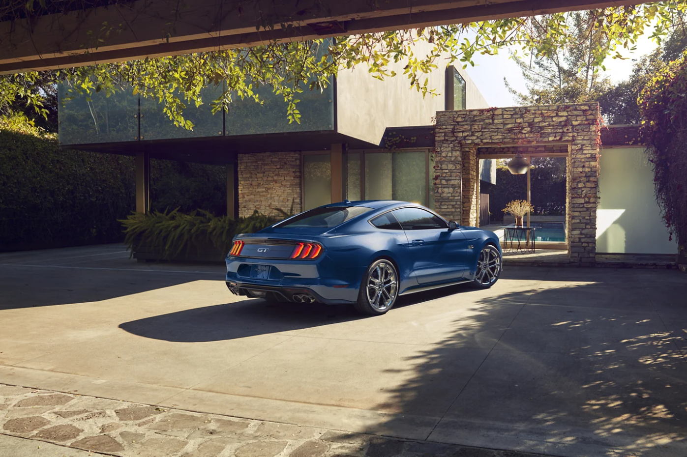 A blue 2022 Ford Mustang sits parked with its nose facing away from the viewer in the driveway of a Midcentury Modern home.