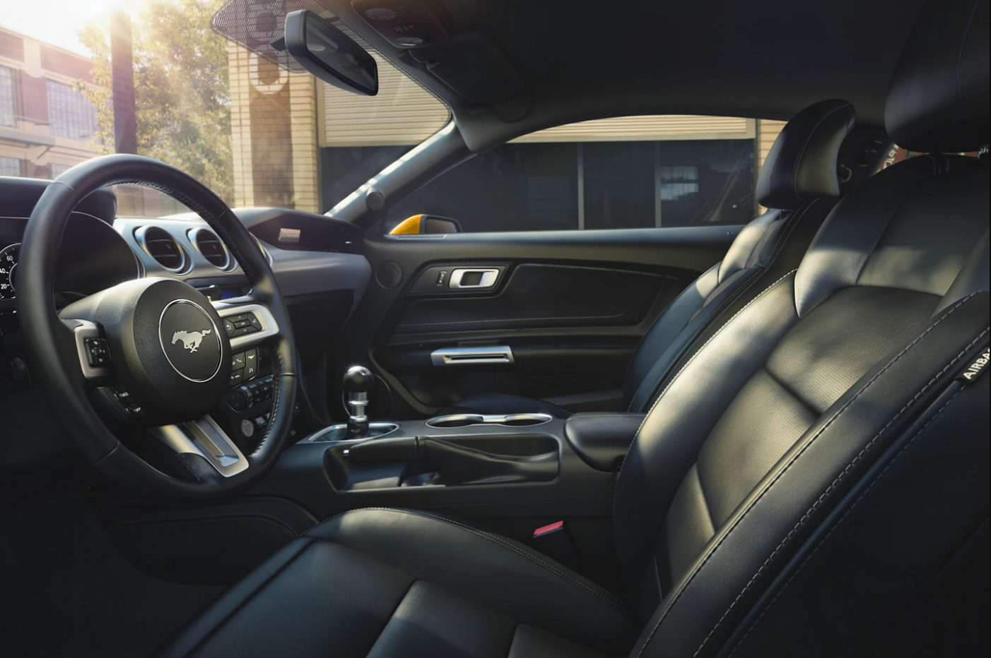 A view of the black leather upholstered interior of a 2022 Ford Mustang from the driver's side showing the seats and Mustang logo on the steering wheel.